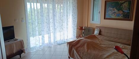 A bedroom with a bed, a television on a side table, a radiator, and a painting on the wall.
