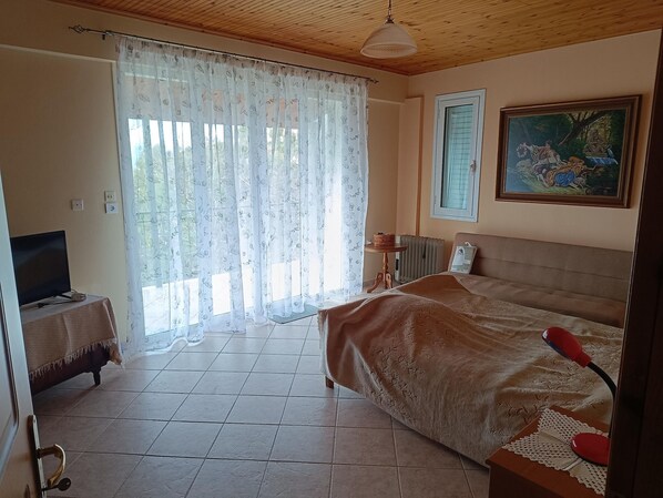 A bedroom with a bed, a television on a side table, a radiator, and a painting on the wall.