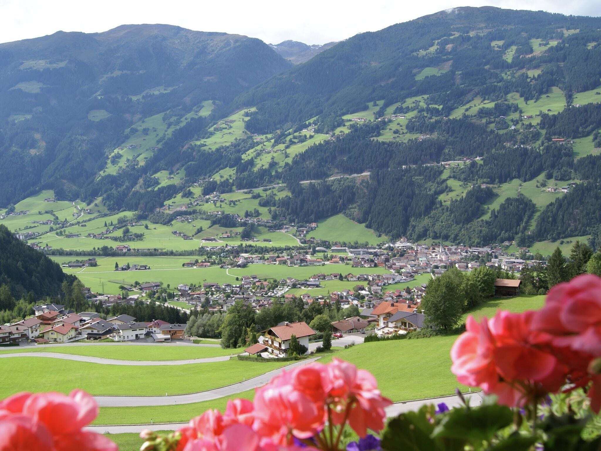 A town nestled in a valley with houses and buildings spread across green fields, surrounded by mountains.