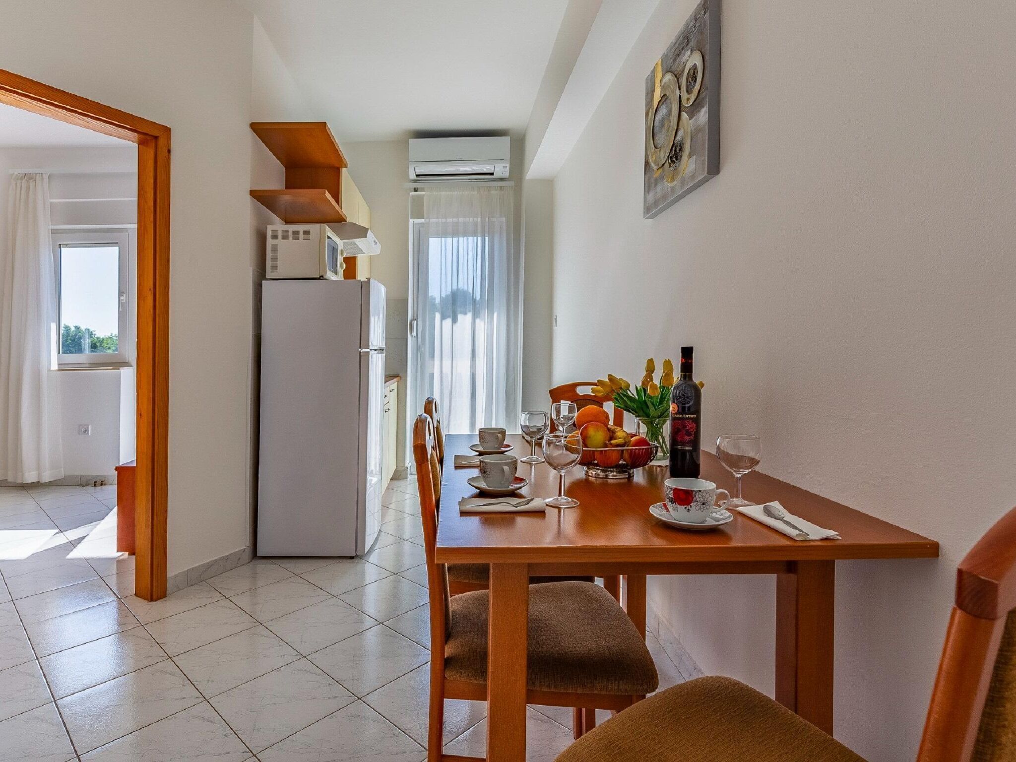 A dining area with a table set for two, a refrigerator, and an air conditioning unit.