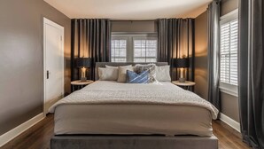 A modern bedroom with a large bed, two bedside tables, and a window with blinds. - Gorgeous 3 Bed Ward Pkwy Home 25 (Kansas City)