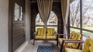 A cozy porch with a yellow armchair, a wooden bench, and a blue rug. - Gorgeous 3 Bed Ward Pkwy Home 25 (Kansas City)