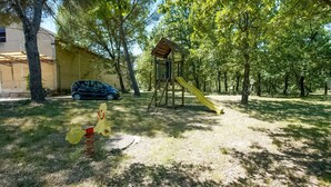 Ein Spielplatz mit Rutsche und Klettergerüst, umgeben von Bäumen und einem parkenden Auto.