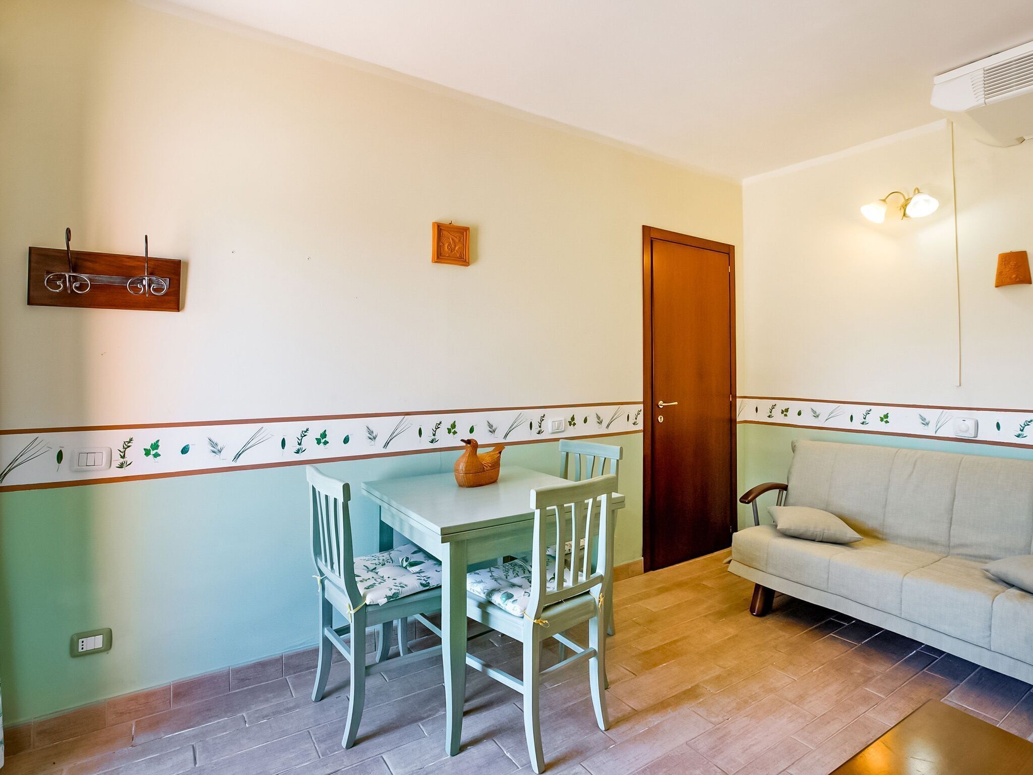 Uma sala de jantar com uma mesa, duas cadeiras, uma porta de madeira e um sofá.