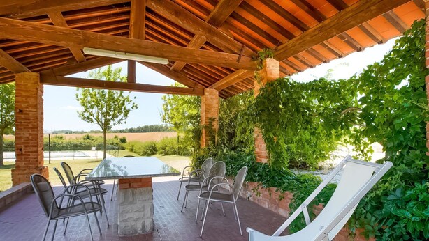 Eine Terrasse im Freien mit Tisch und Stühlen, umgeben von Grün und Blick auf die Landschaft.