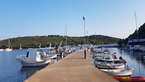 Ein Yachthafen mit Booten, die an einer Betonpier liegen, umgeben von Wasser und einer hügeligen Landschaft.