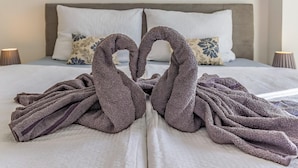 Ein ordentlich gemachtes Bett mit Kopfstütze, zwei Kissen und ein Paar Handtücher, die in Herzform drapiert sind.