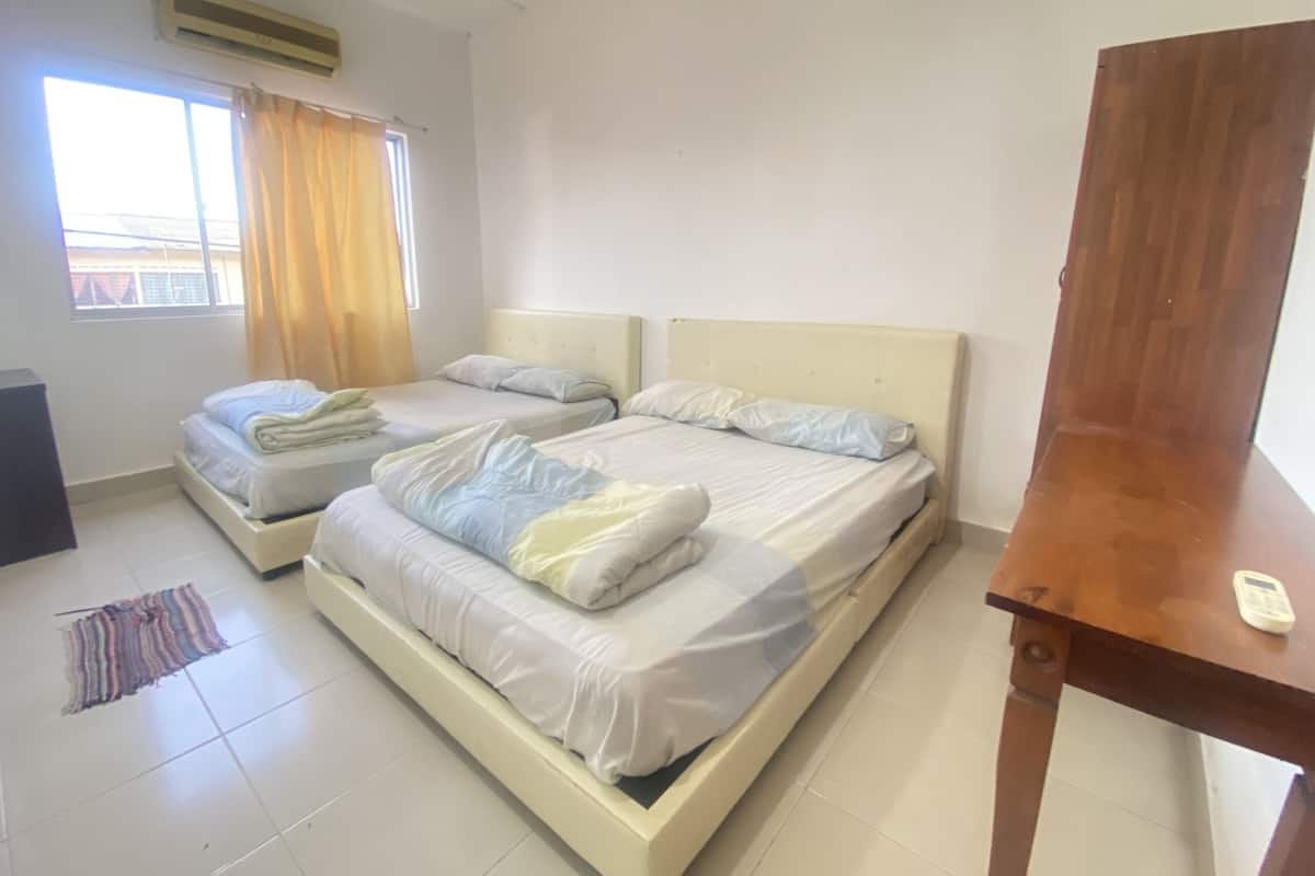 A room with two beds, a window with curtains, a wooden table, and a speaker.