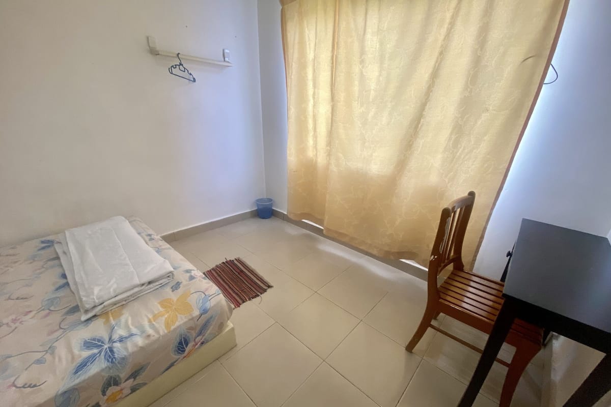 A bedroom with a bed, a chair, a desk, a curtain, and a wall-mounted shelf.