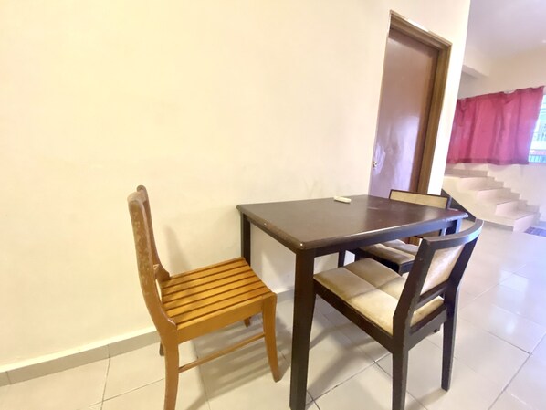 A dining area with a wooden table and chairs, a remote control on the table, and a staircase in the background.