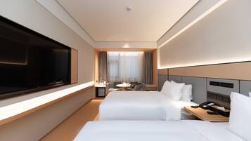 Quarto de hotel com duas camas, televisão, mesa com telefone e uma pequena mesa com cadeira.