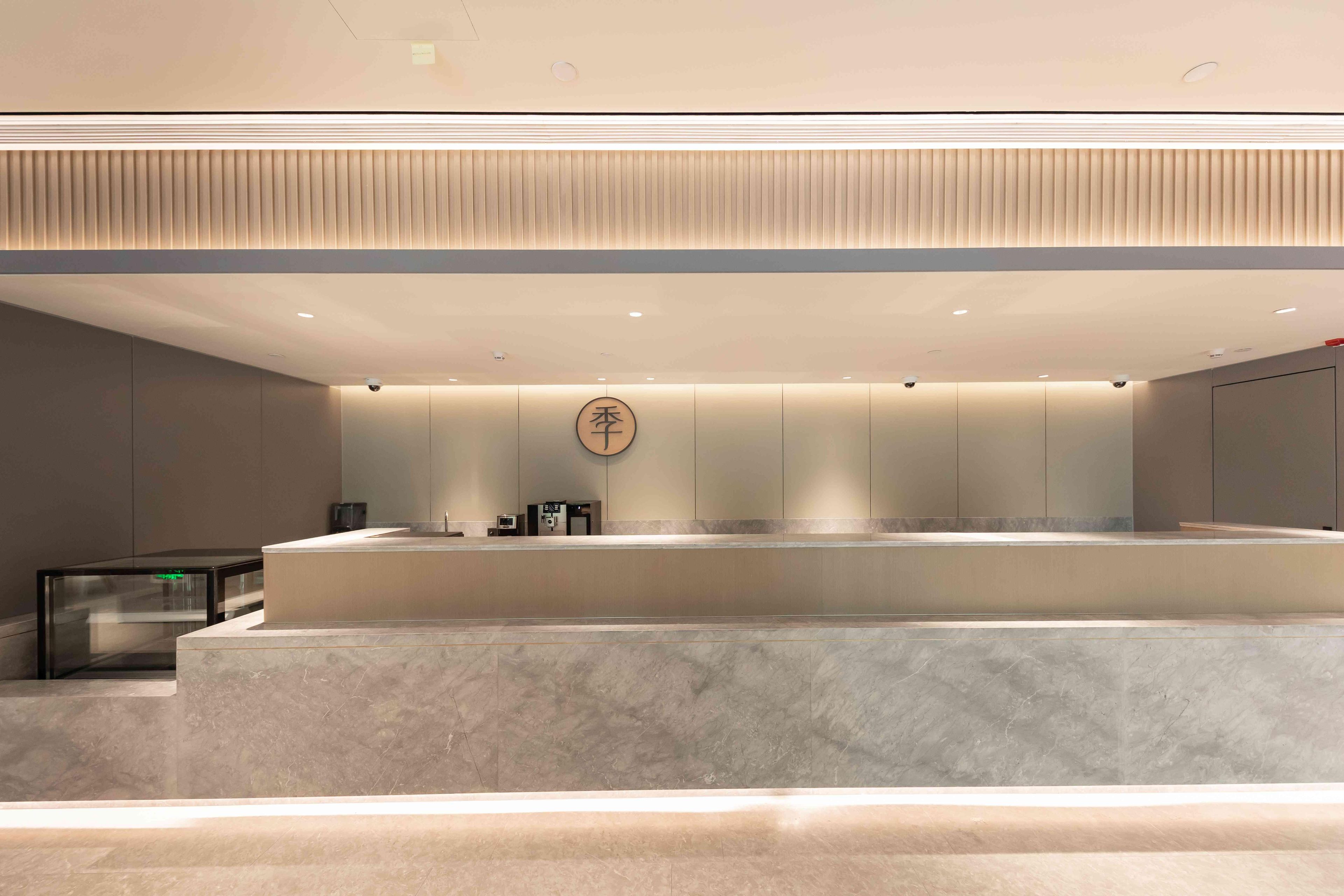 A modern hotel lobby with a reception desk, a security camera, and a logo on the wall.