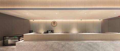 A modern hotel lobby with a reception desk, a security camera, and a logo on the wall.