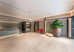 A modern interior with a reception desk, a large potted plant, and a red chair. - Ji Hotel (Shanghai)