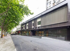 Um hotel com fachada moderna, entrada visível e rua arborizada.