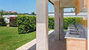 A modern outdoor kitchen area with a sink and a built-in grill, surrounded by a well-maintained garden and a clear blue sky. - Mobile Home in Banjole near Beach Centinera (Banjole)