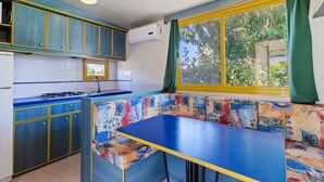 A compact kitchen with blue cabinets, a gas stove, and a window with green curtains. - Mobile Home in Banjole near Beach Centinera (Banjole)