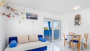 A room with a blue sofa, a dining table with chairs, a large window, and a wall with nautical decorations. - Mandre Coastal Hideaway (Mandre)
