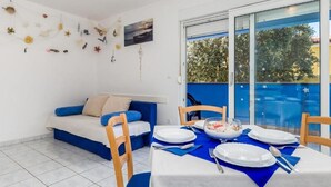 A room with a dining table set for four, a sofa with blue cushions, and a wall decorated with various items. - Mandre Coastal Hideaway (Mandre)