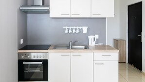 Une cuisine moderne avec des meubles blancs, un four en acier inoxydable, un évier et une bouilloire.