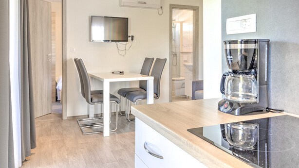 A modern kitchen with a coffee maker, a TV mounted on the wall, and a dining area with chairs and a table. - Mobile Home in Banjole near Beach & Pool (Banjole)