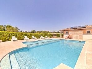 Une piscine dotée de chaises longues et d’un toboggan, entourée d’un jardin aménagé et d’un bâtiment dont le toit est recouvert de tuiles.