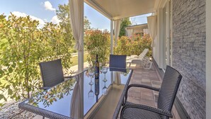 A covered outdoor seating area with a glass table and wicker chairs, overlooking a garden with trees and shrubs. - Mobile Home in Banjole near Beach & Pool (Banjole)