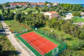 Vista aérea de una cancha de tenis rodeada de zonas verdes y edificios residenciales.