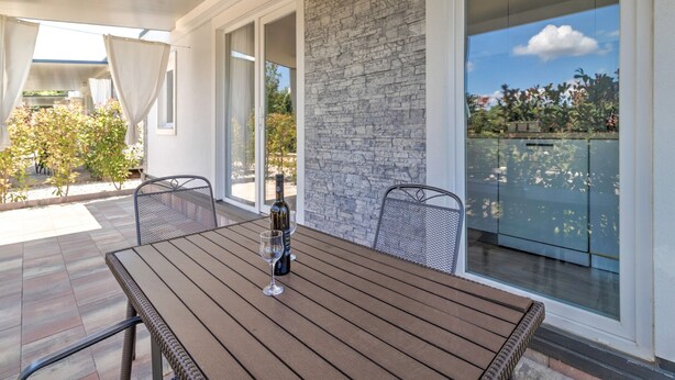 An outdoor patio with a wooden table, two chairs, a bottle of wine, and a glass. - Mobile Home in Banjole near Beach (Banjole)
