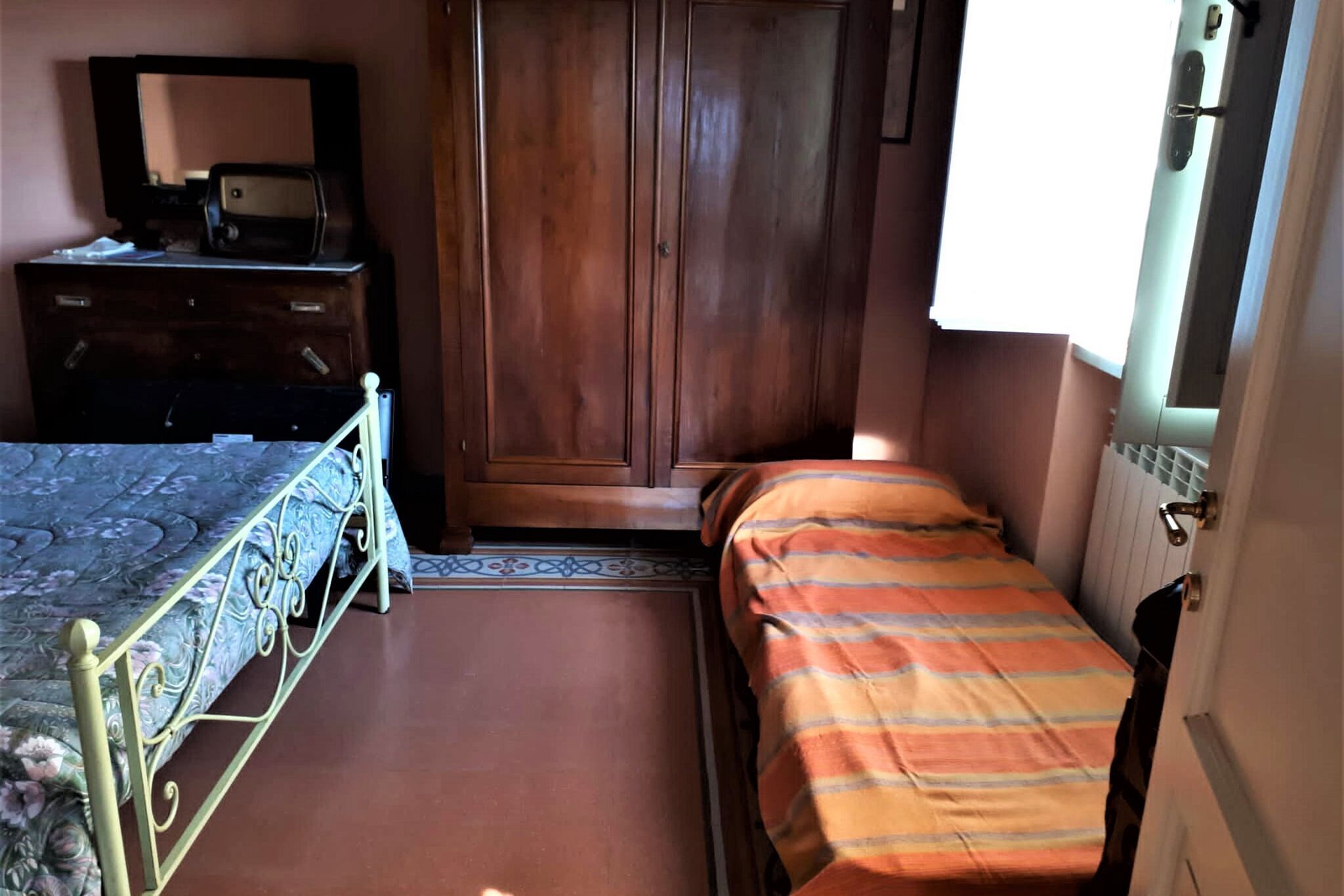 Une chambre à coucher avec un lit, une commode, une armoire et une fenêtre.
