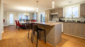 A modern kitchen with wooden cabinets, a large island, and pendant lighting. - Maison des Champs (Saint-Jean-de-l'Île-d'Orléans)