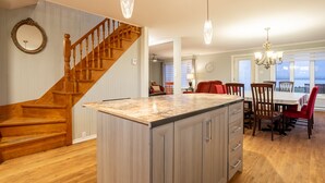A spacious kitchen with a wooden staircase, a marble island, and a dining area with red chairs. - Maison des Champs (Saint-Jean-de-l'Île-d'Orléans)