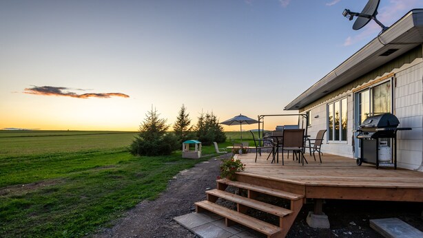 A patio with outdoor furniture, a grill, and a view of the countryside at sunset. - Maison des Champs (Saint-Jean-de-l'Île-d'Orléans)