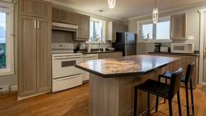 A modern kitchen with wooden cabinets, stainless steel appliances, and a granite island. - Maison des Champs (Saint-Jean-de-l'Île-d'Orléans)