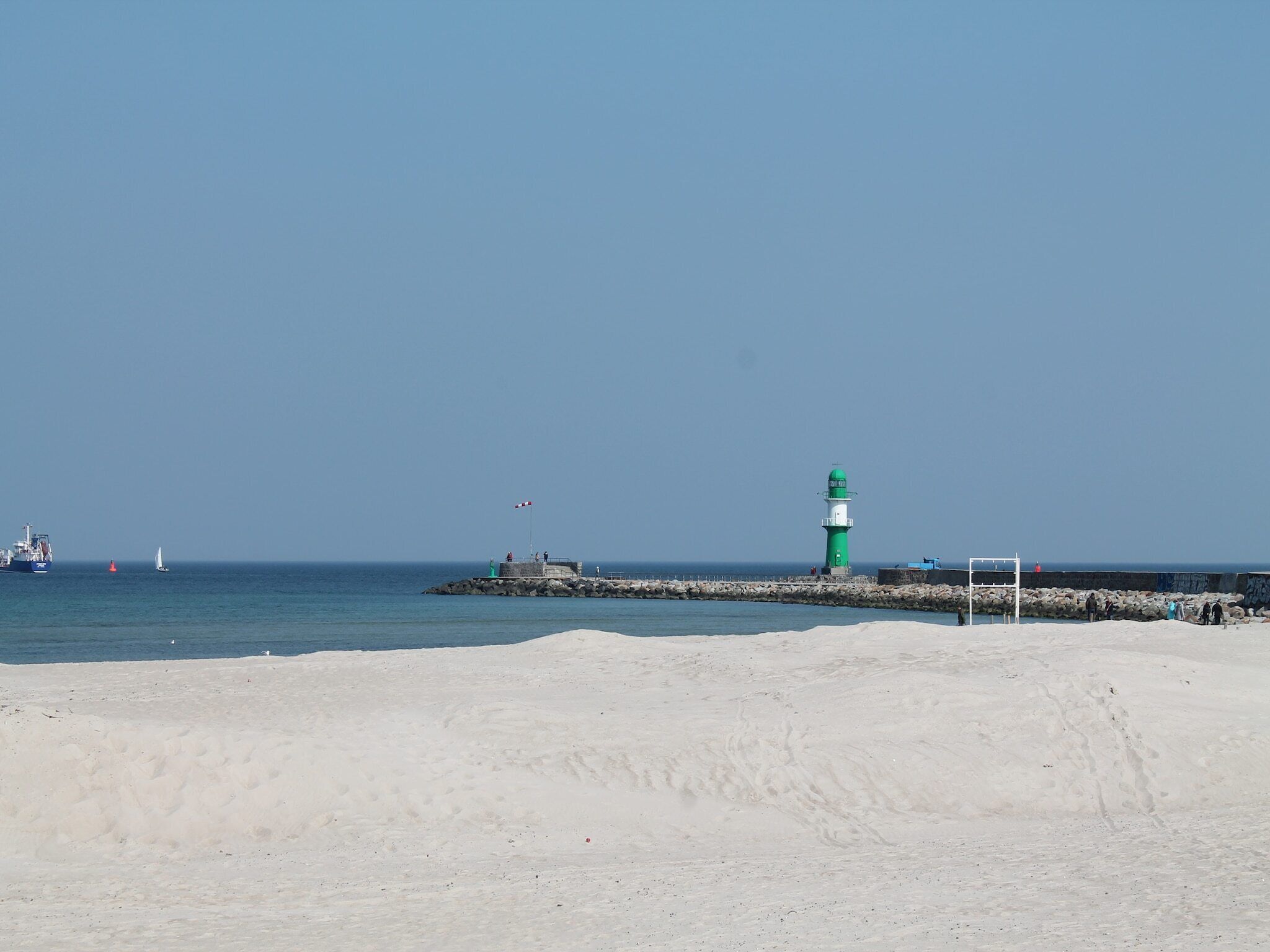 Um farol sobre um cais, com uma praia arenosa em primeiro plano.