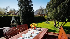 A wooden deck with a table set for two, surrounded by chairs, and a grill in the background. - Cozy Baltic Escape for 2 Guests (Bastorf / Kägsdorf)