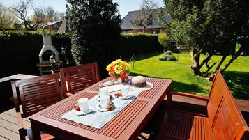 Un patio in legno con un tavolo apparecchiato per due, circondato da sedie, e un barbecue sullo sfondo.