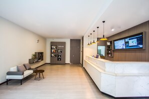 Una zona d'entrada moderna amb un taulell de marbre, un espai d'estar amb sofà i cadires, i un televisor penjat a la paret.