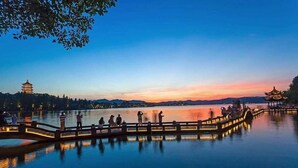 A serene lakeside scene with a traditional pagoda and a wooden bridge.