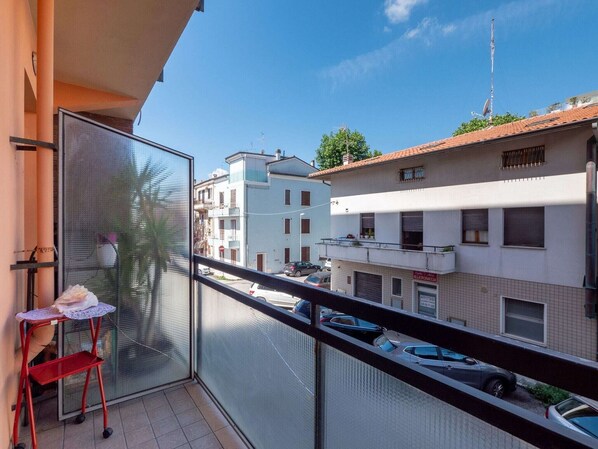 A balcony with a red chair and a small table, overlooking a street with parked cars and buildings. - Holiday Home in Fano near the Beach (Fano)