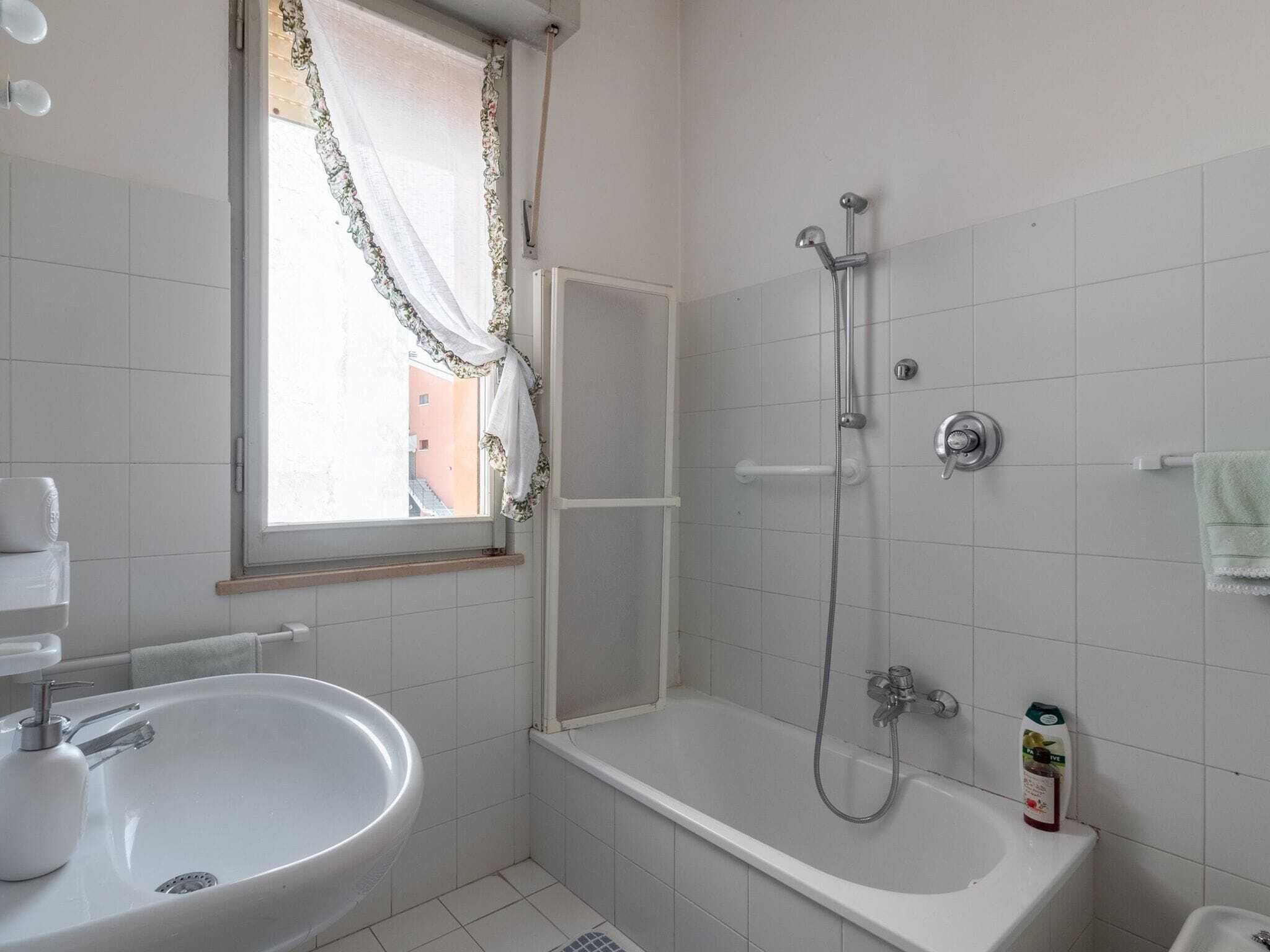 Un bagno con un lavandino bianco, una doccia e una finestra con tenda a fiori.