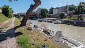 Un canal bordé de bateaux amarrés, un sentier longeant l’eau et des bâtiments en arrière-plan.