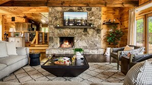 L’intérieur chaleureux d’un chalet en rondins, avec une cheminée en pierre, un plafond en bois et des coins salon confortables.