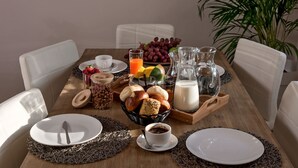A breakfast table with plates, cups, a basket of bread, a fruit bowl, and a pitcher of milk.