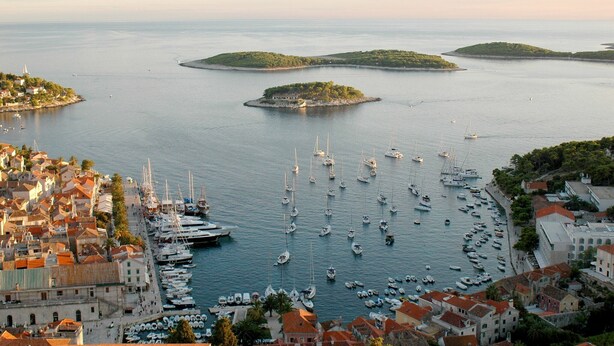 A coastal town with a marina filled with boats, surrounded by buildings and small islands.