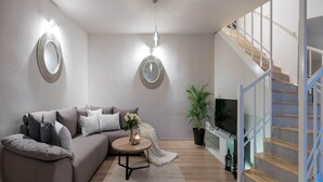 A modern living room with a grey sofa, round mirrors, a wooden coffee table, and a staircase with wooden steps and blue railings.
