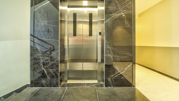An elevator with a metallic finish and a glass panel, surrounded by marble walls with visible cracks. - Treebo Sriz Cozy Seethamadhara (Visakhapatnam)