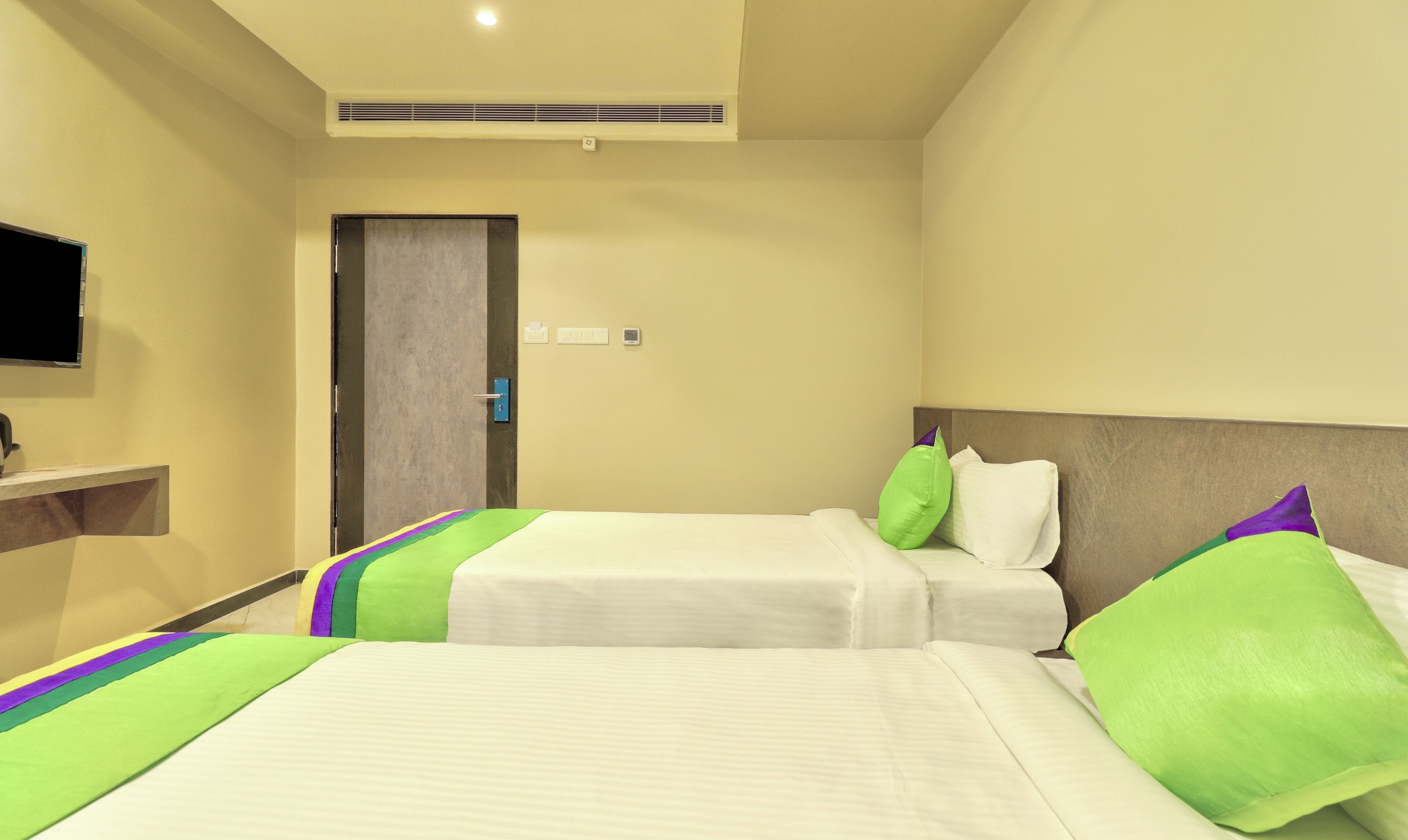 A hotel room with two beds, a TV mounted on the wall, and a door.