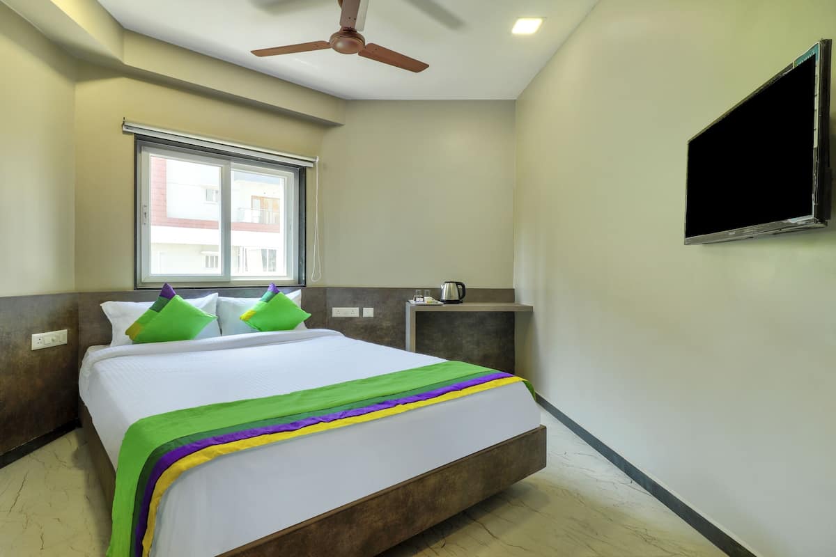 Ein Hotelzimmer mit einem Bett, einem Deckenventilator, einem Fenster, einem Flachbildfernseher und einem kleinen Tisch mit einem Wasserkocher.
