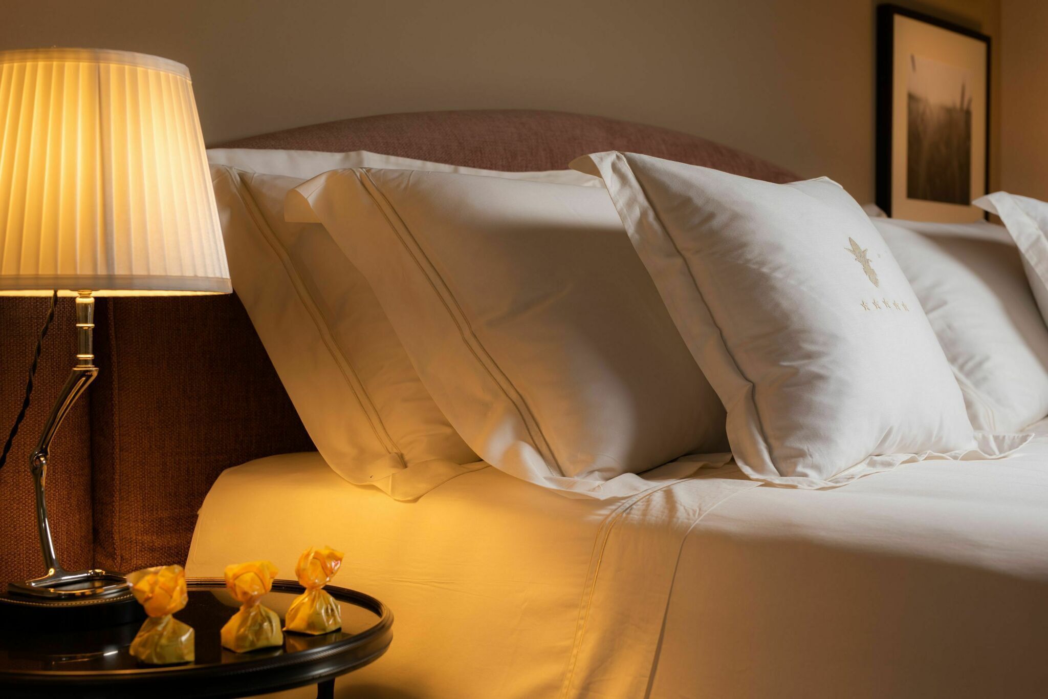 A neatly made bed with white linens and pillows, a bedside lamp, and a small tray with decorative items.